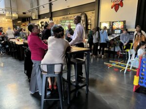 Several adults gathered at a table, with youth in the background playing pinball and other games.